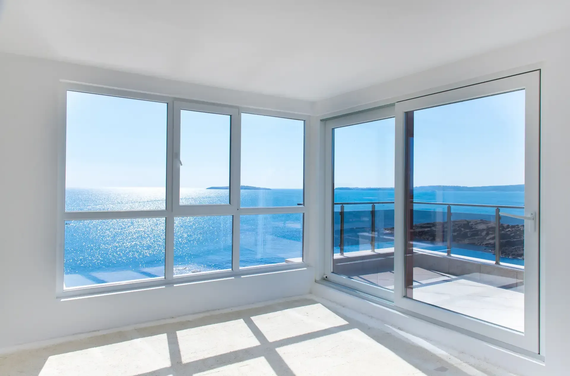 Bright room with large windows overlooking a blue ocean and sunny balcony