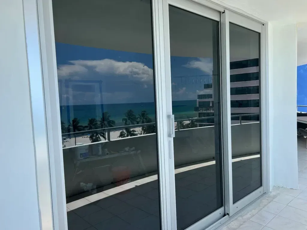 Glass sliding doors reflecting ocean and palm trees on a sunny balcony