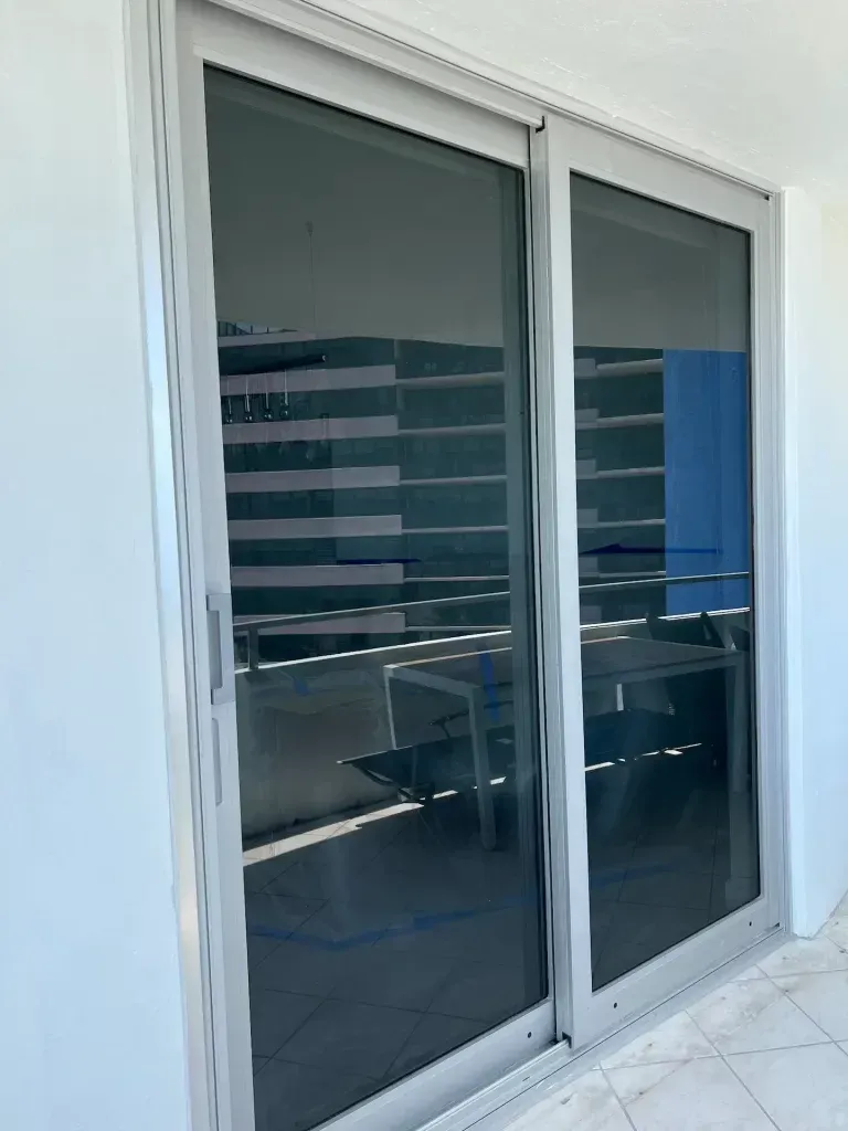 Sliding glass doors with dark tinted panels reflecting an office interior and chairs