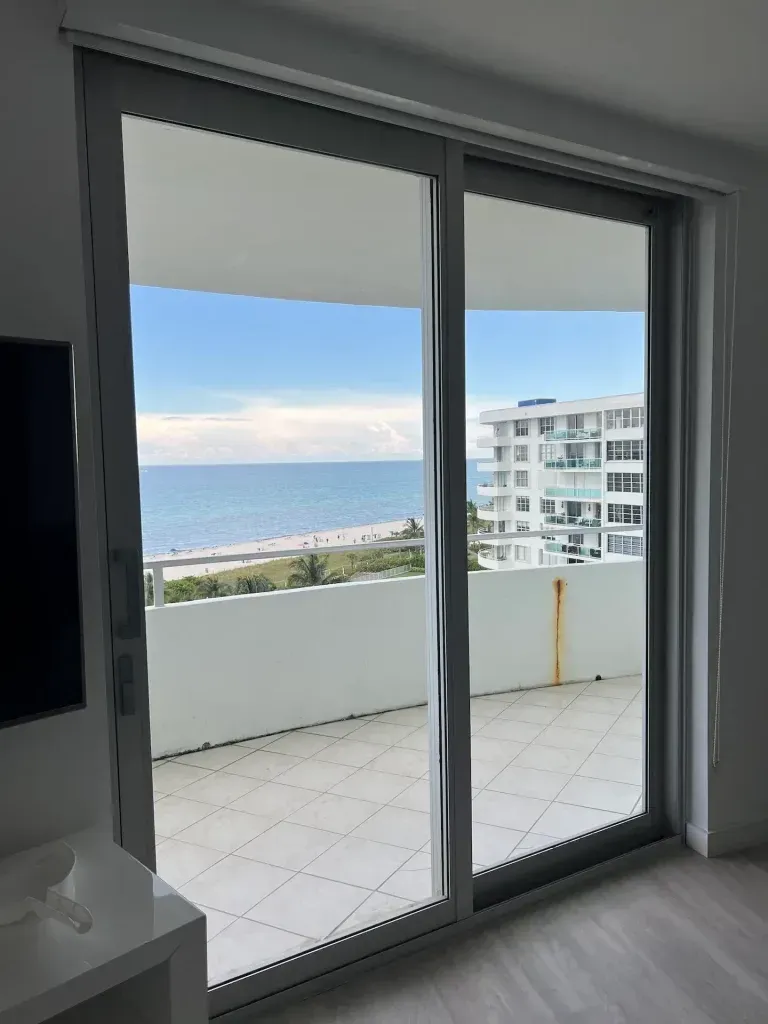 Balcony view through sliding glass doors toward the ocean and a neighboring building