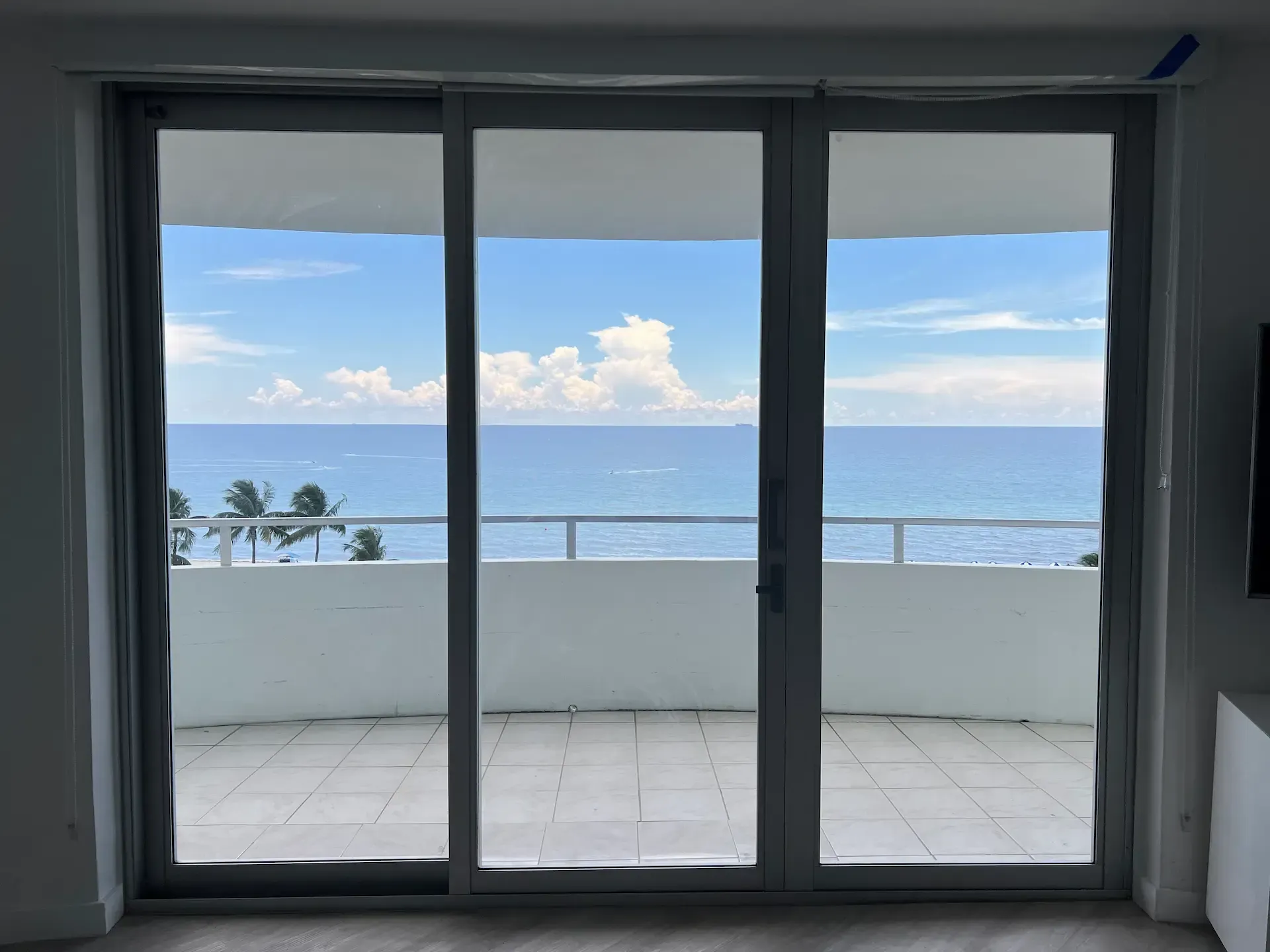 Sliding glass doors open to a balcony with ocean view and blue sky