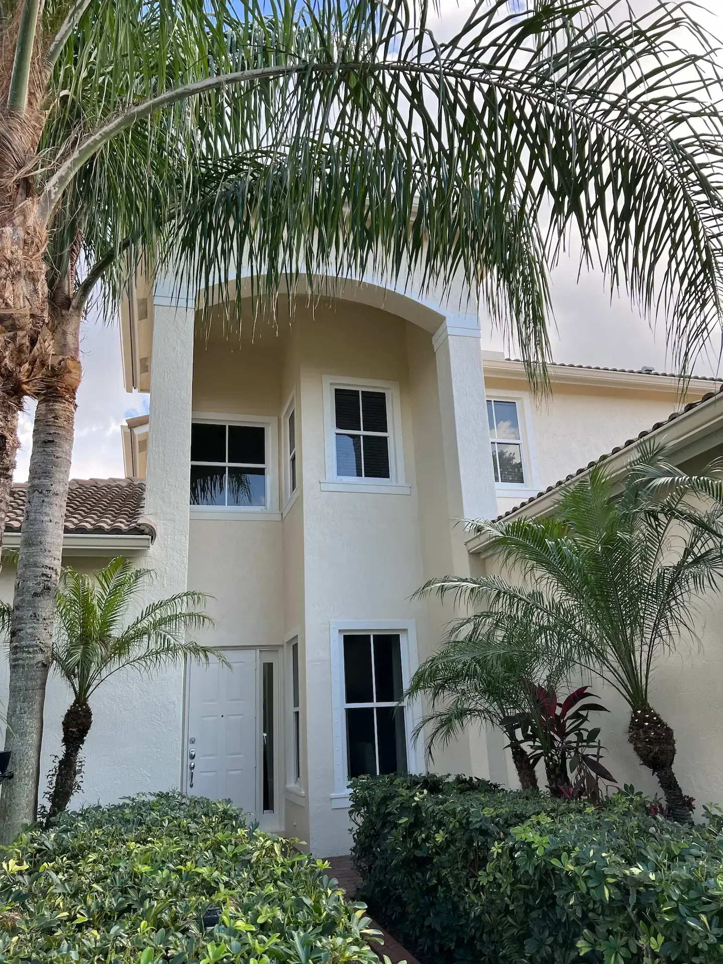 Cream-colored two-story house with arched entrance, white windows, and palm trees in front