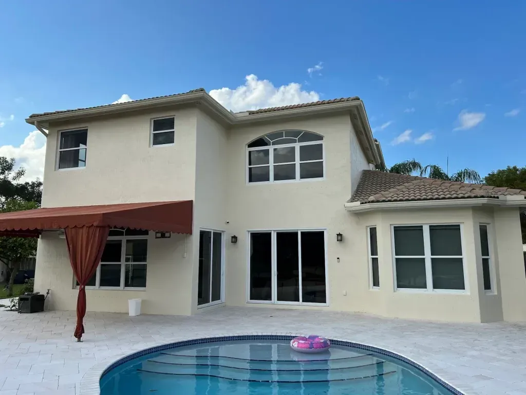 Two-story beige house with a red patio awning and a backyard pool under a blue sky