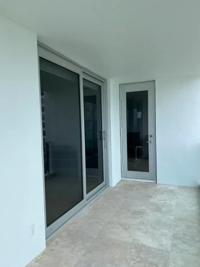 Empty patio with large sliding glass door and narrow exterior door leading to a modern interior.