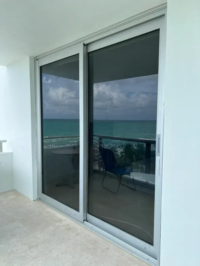 Sliding glass doors opening to a balcony with ocean view and patio chairs