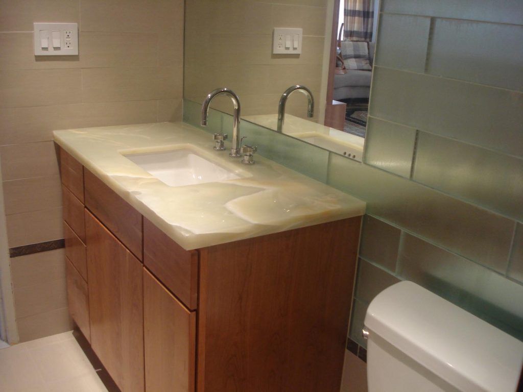 Modern bathroom vanity with double sink, wooden cabinet, mirror, and toilet beside a frosted glass shower.