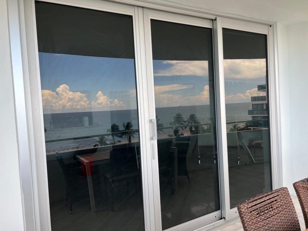 Sliding glass balcony doors reflecting the ocean and sky at sunset