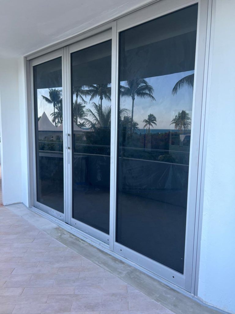 Sliding glass patio doors with dark tinted panels on a white exterior wall, reflecting palm trees.