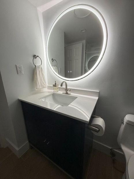 Modern bathroom vanity with illuminated round mirror, white sink, and dark cabinet