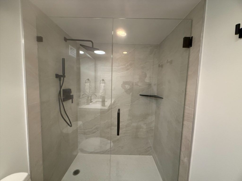 Modern glass shower enclosure with rain shower head, handheld sprayer, and built-in shelf in a bright bathroom