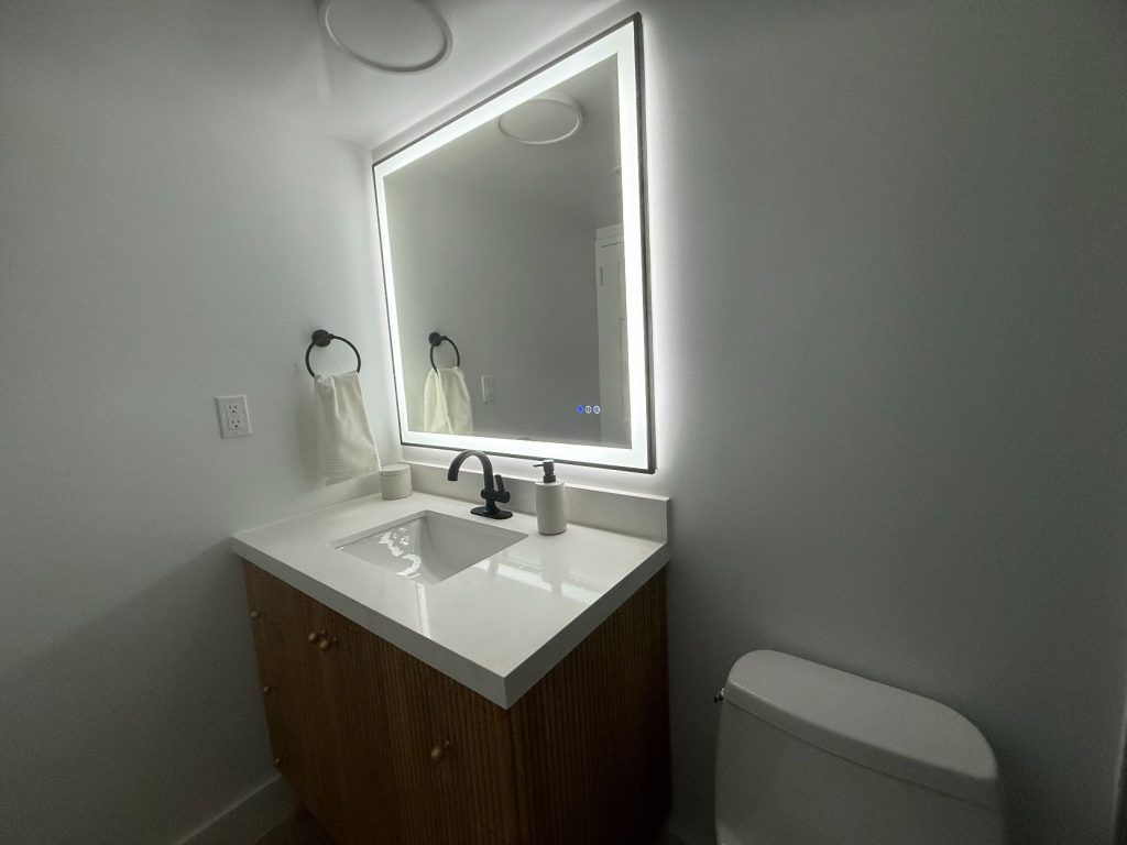 Modern bathroom with backlit mirror, white vanity, and toilet on the right