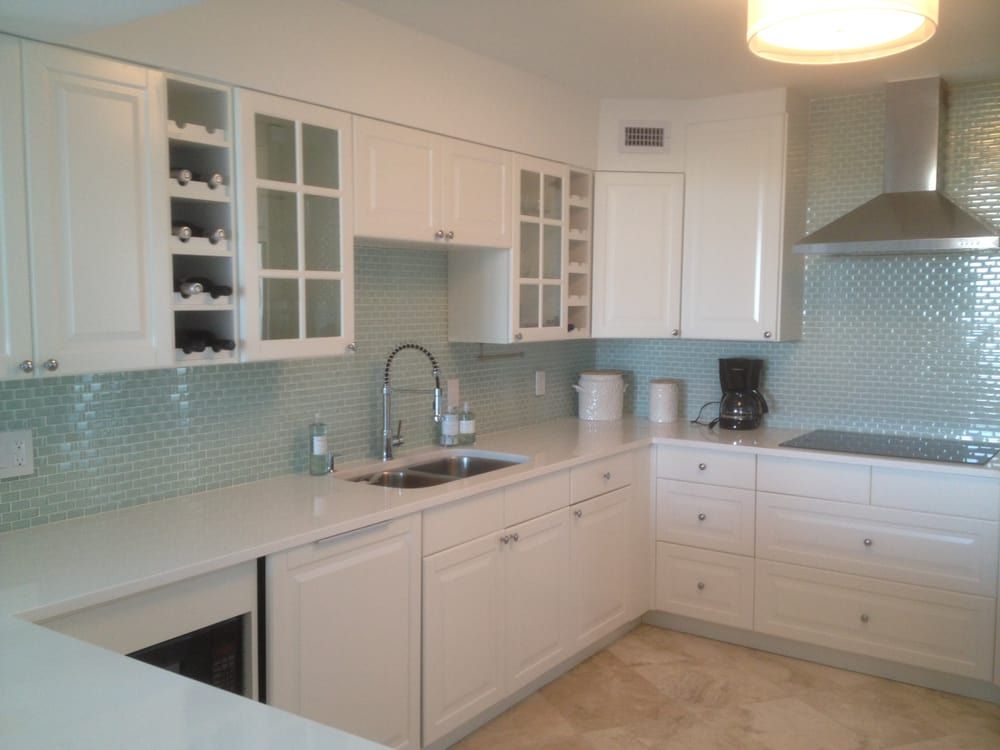 Bright white modern kitchen with light blue tile backsplash and stainless steel range hood