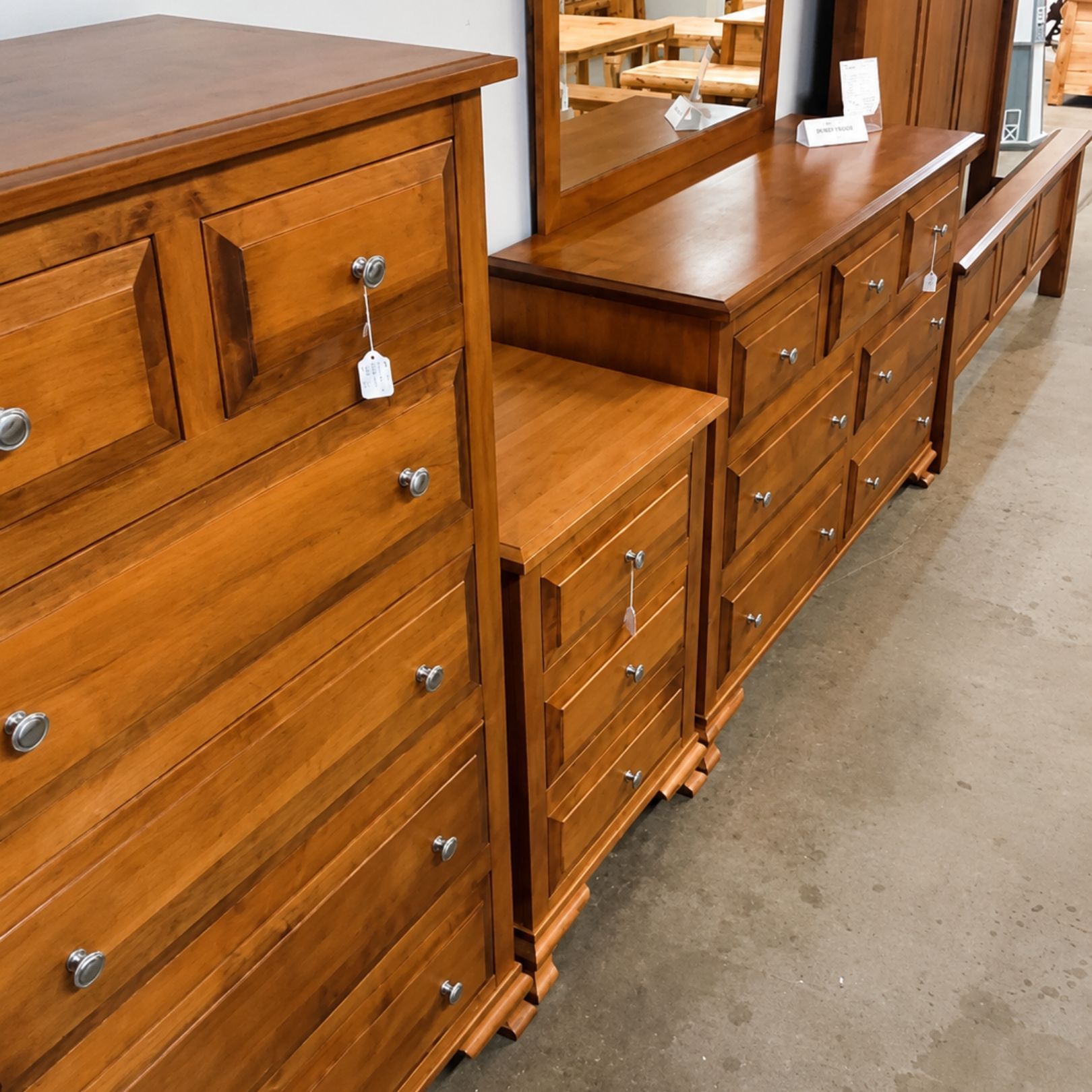 Row of wooden dressers and cabinets in a store showroom, with a mirror visible above one piece.