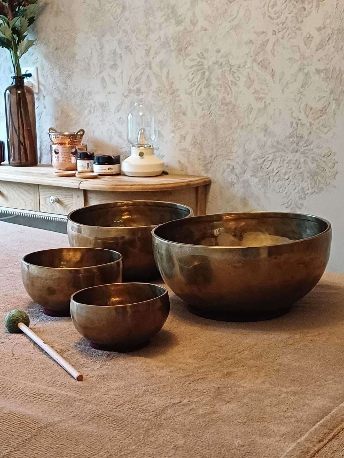Messing klankschalen en een hamer op een met jute bedekte tafel in een rustige, rustieke kamer.