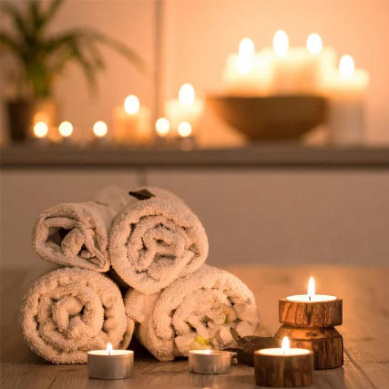 Opgerolde handdoeken en brandende kaarsen in een spa-achtige omgeving met warme, zachte verlichting.