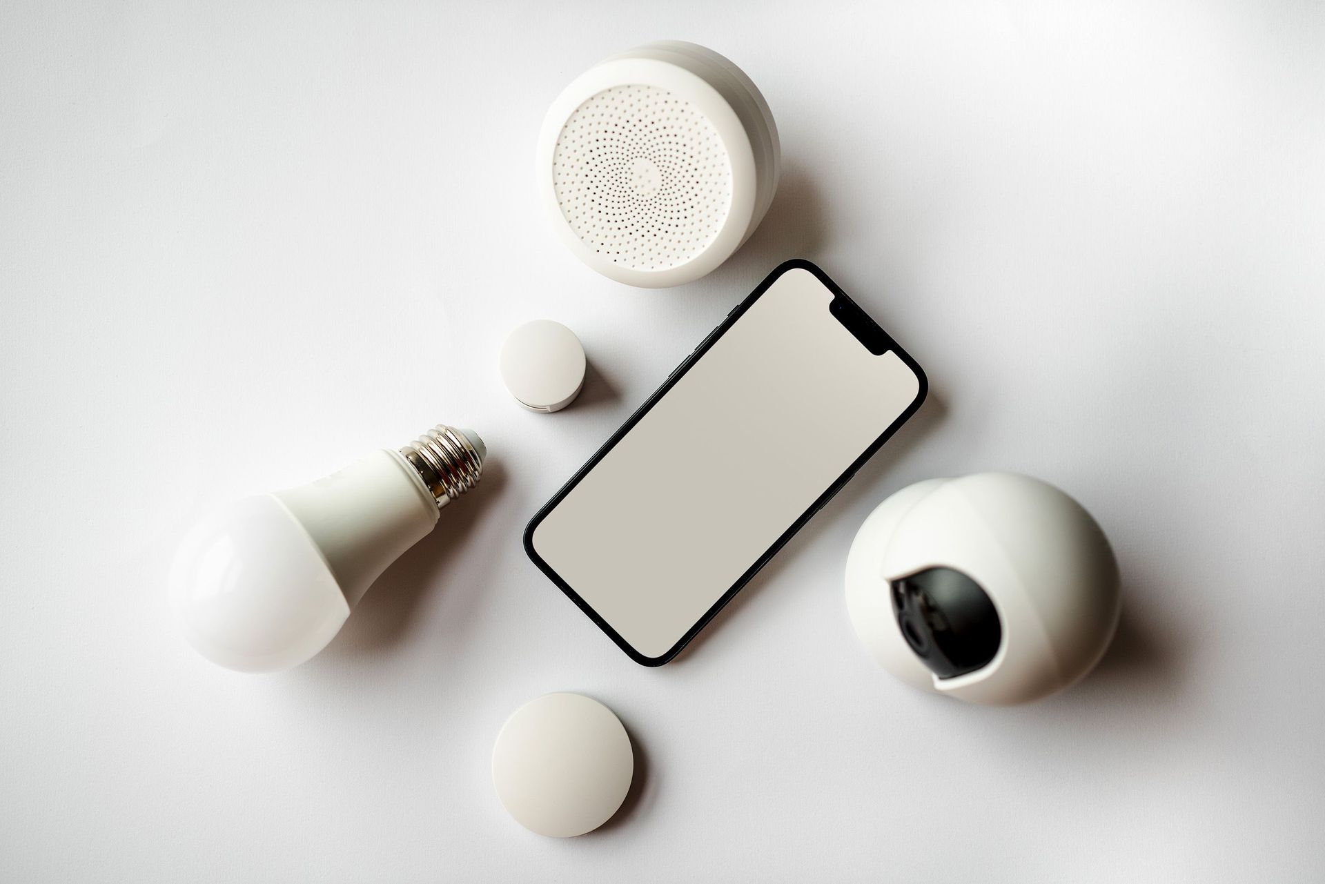 Flat lay of a smartphone surrounded by white smart home devices on a light background