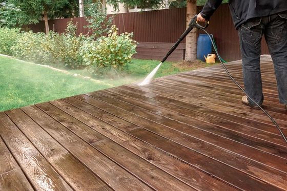 Man cleaning walls and floor with high pressure power washer. Washing terrace wood planks and cladding walls