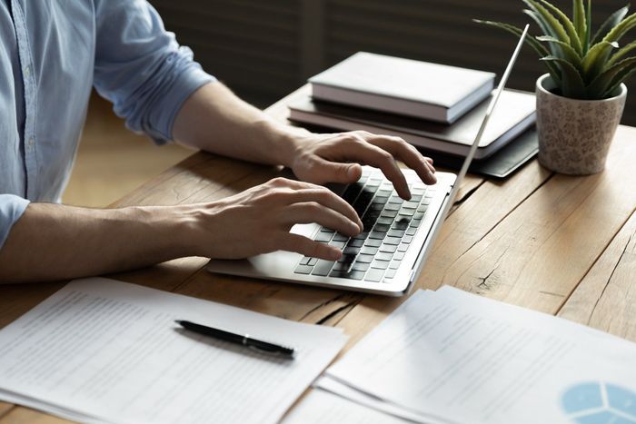 A Man is Typing on a Laptop Computer at a Desk — Coastal Computing Solutions in Taree, NSW