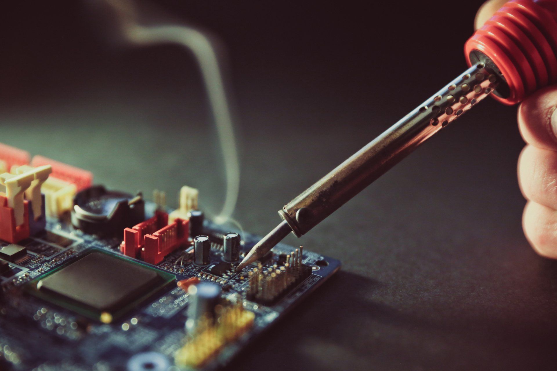 A Person is Soldering a Motherboard With a Soldering Iron — Coastal Computing Solutions in Taree, NSW