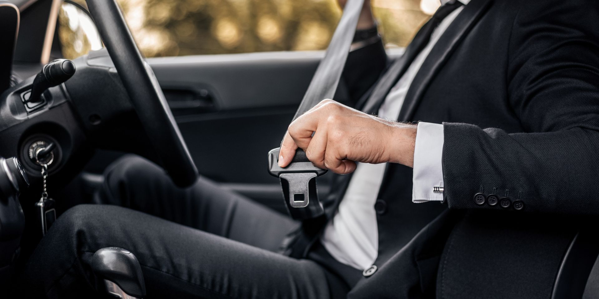 A person wearing a suit buckles their seatbelt while sitting in the driver's seat of a car.