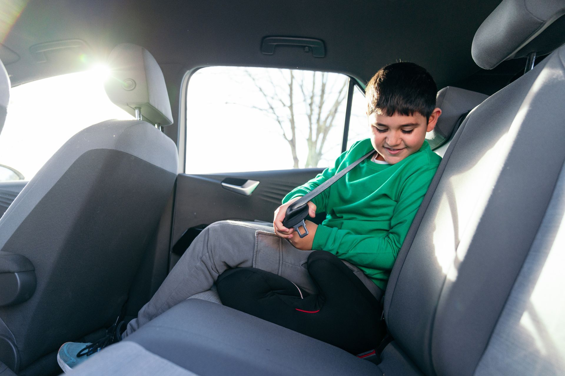 A person in a green sweater sits in the back of a car, reaching to pull a seatbelt across their torso.