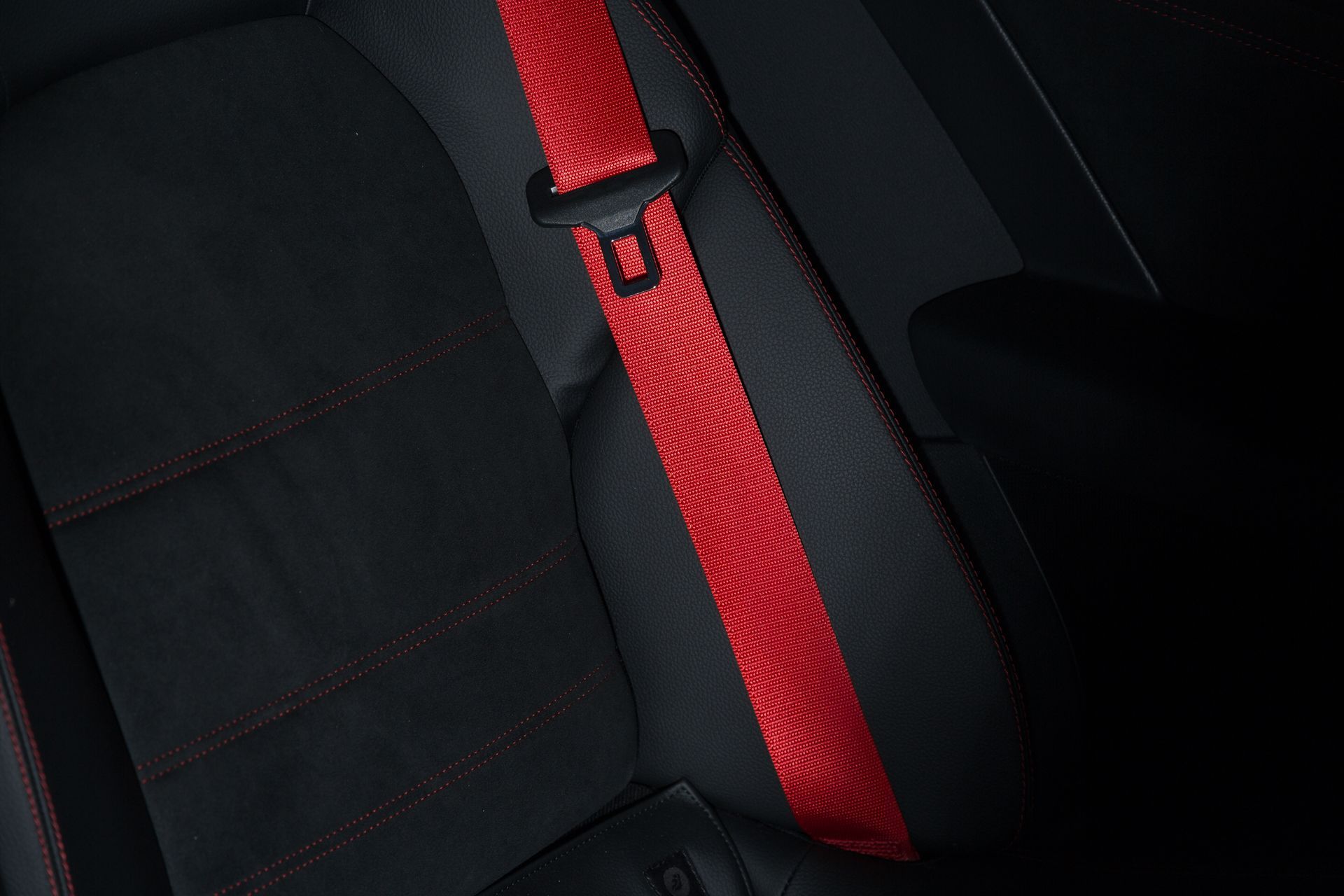 A vibrant red seatbelt with a textured pattern resting against a black car seat with red stitching.
