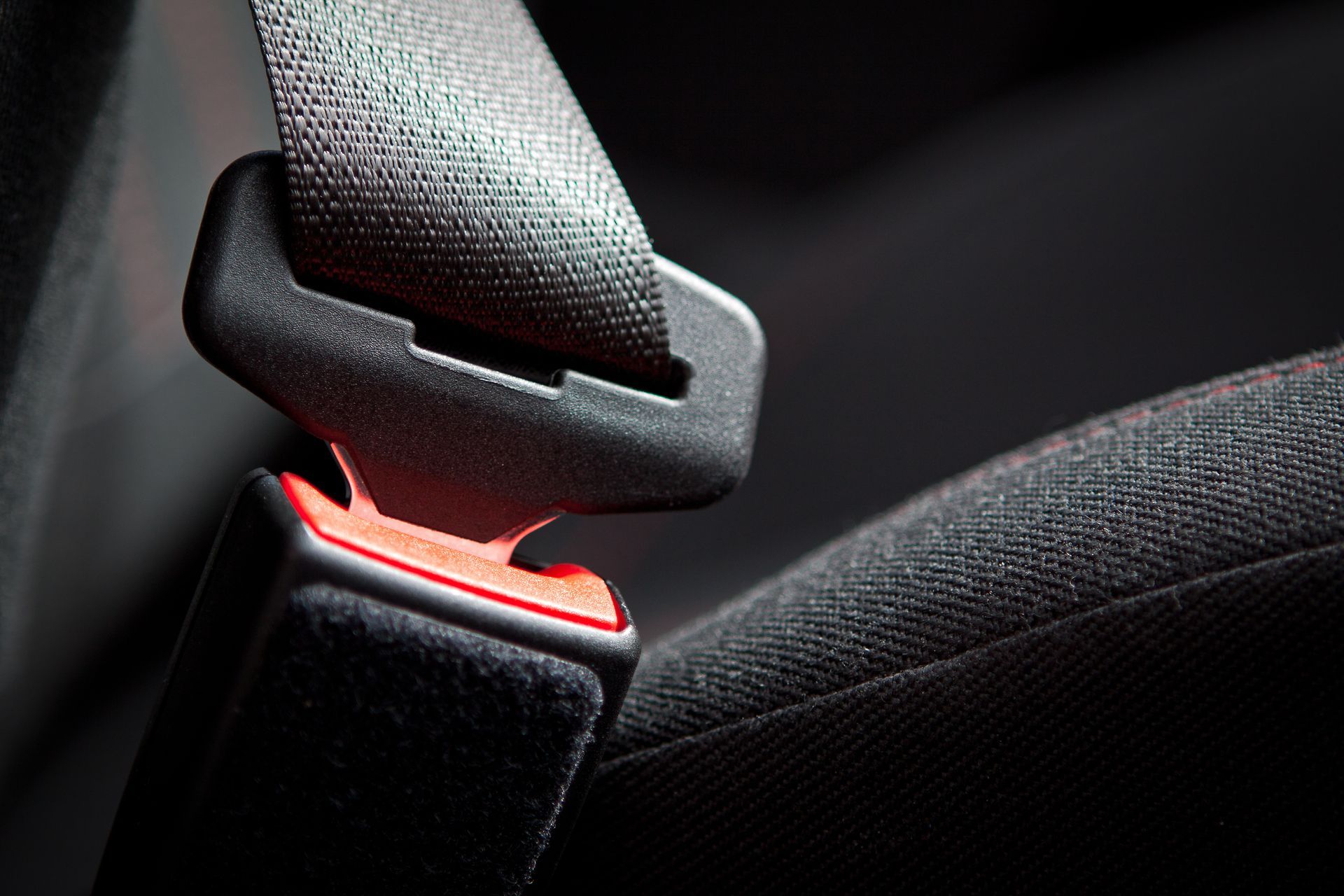 A black car seat belt fastened into a black buckle with a small red release button.