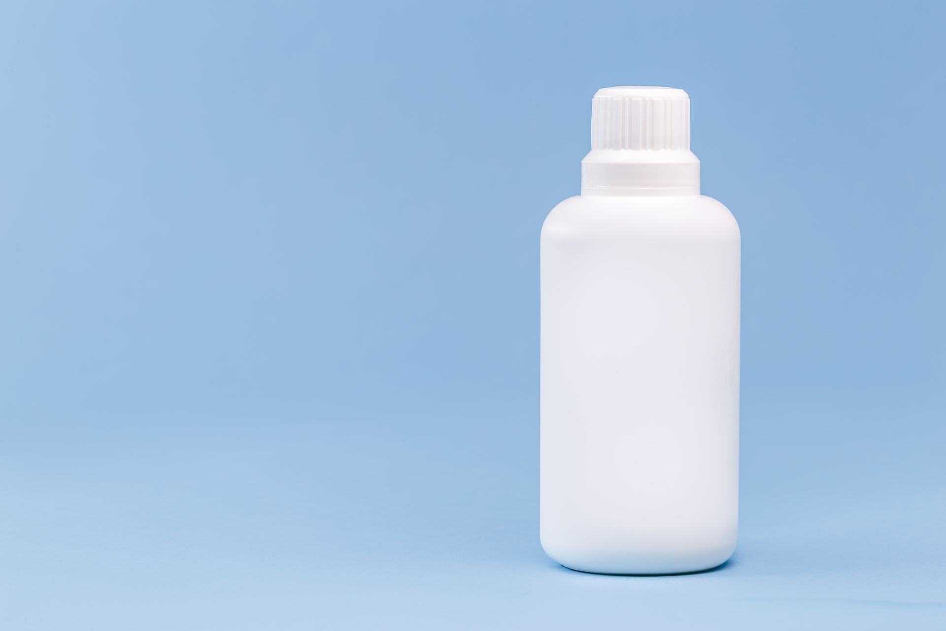 A white, empty plastic bottle with a screw-top cap, centered against a plain light blue background.