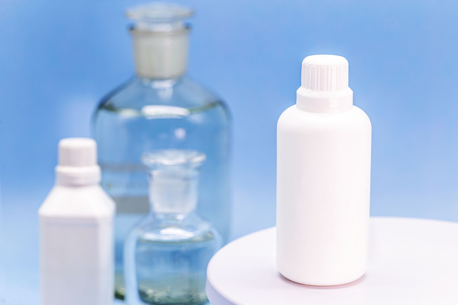 A white bottle stands on a pedestal in the foreground, with glass chemical bottles blurred in the background.