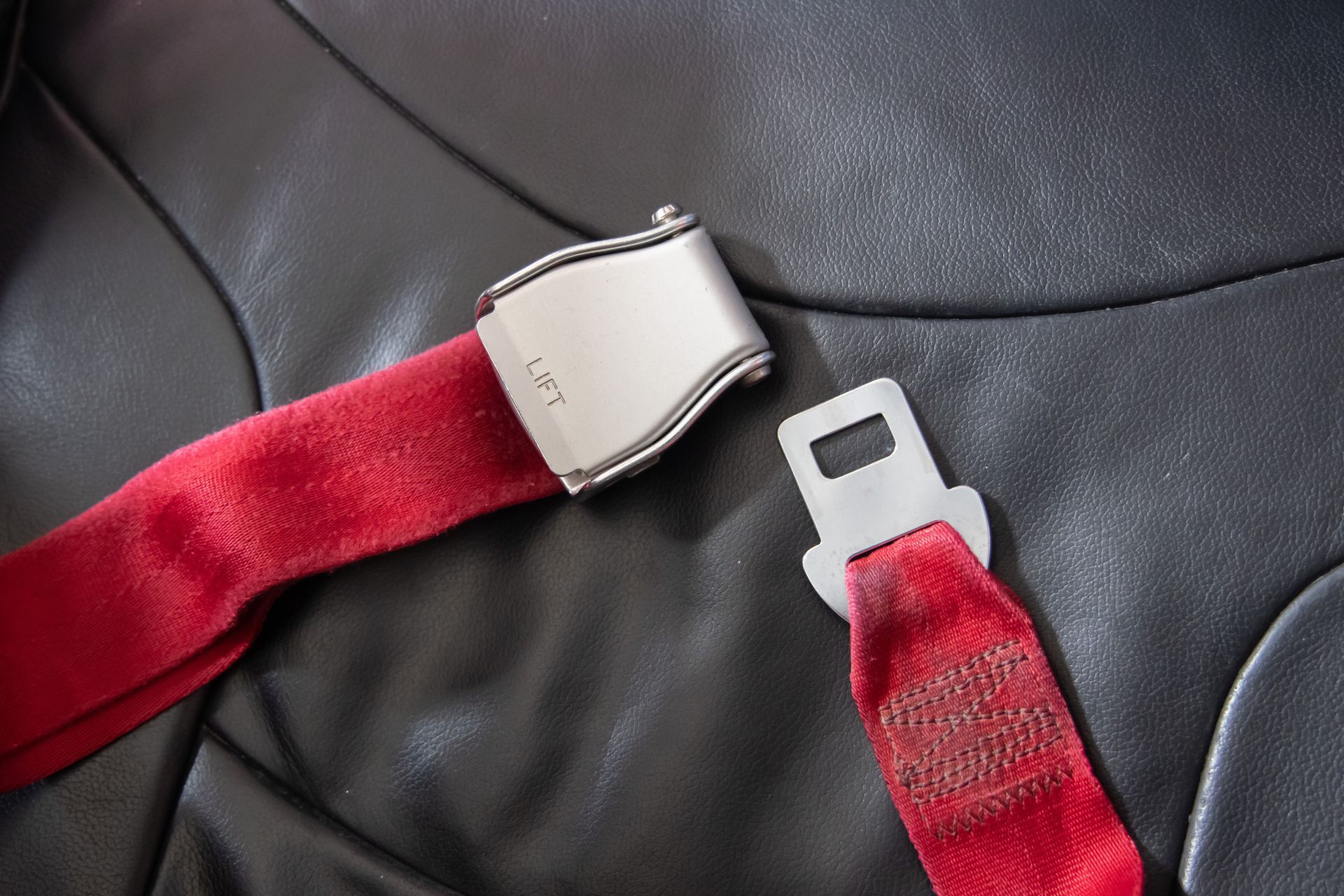 Seatbelt with a metal buckle and tongue resting on a dark leather seat.