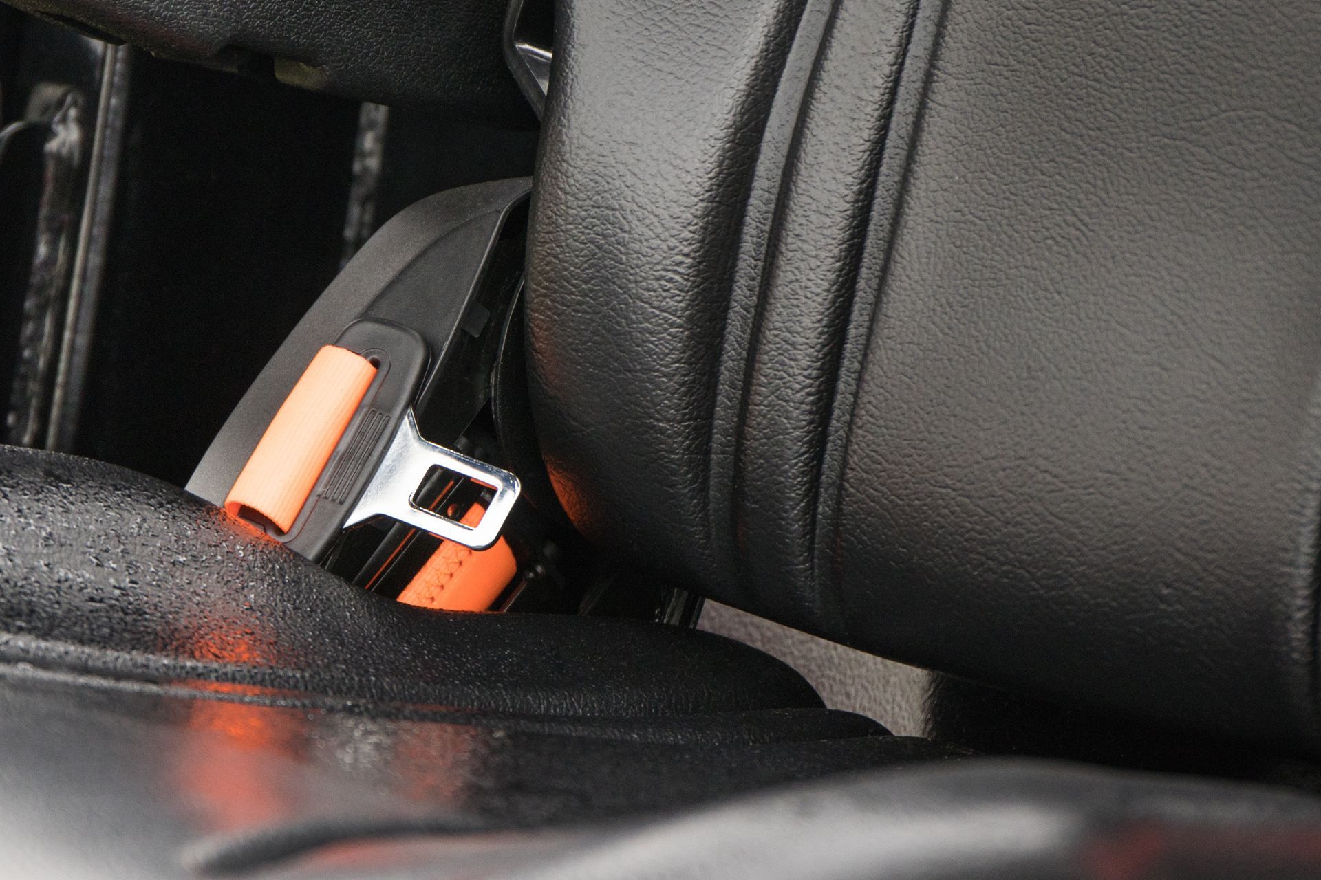 Close-up of a vibrant orange seat belt buckle fastened against a textured black car seat.
