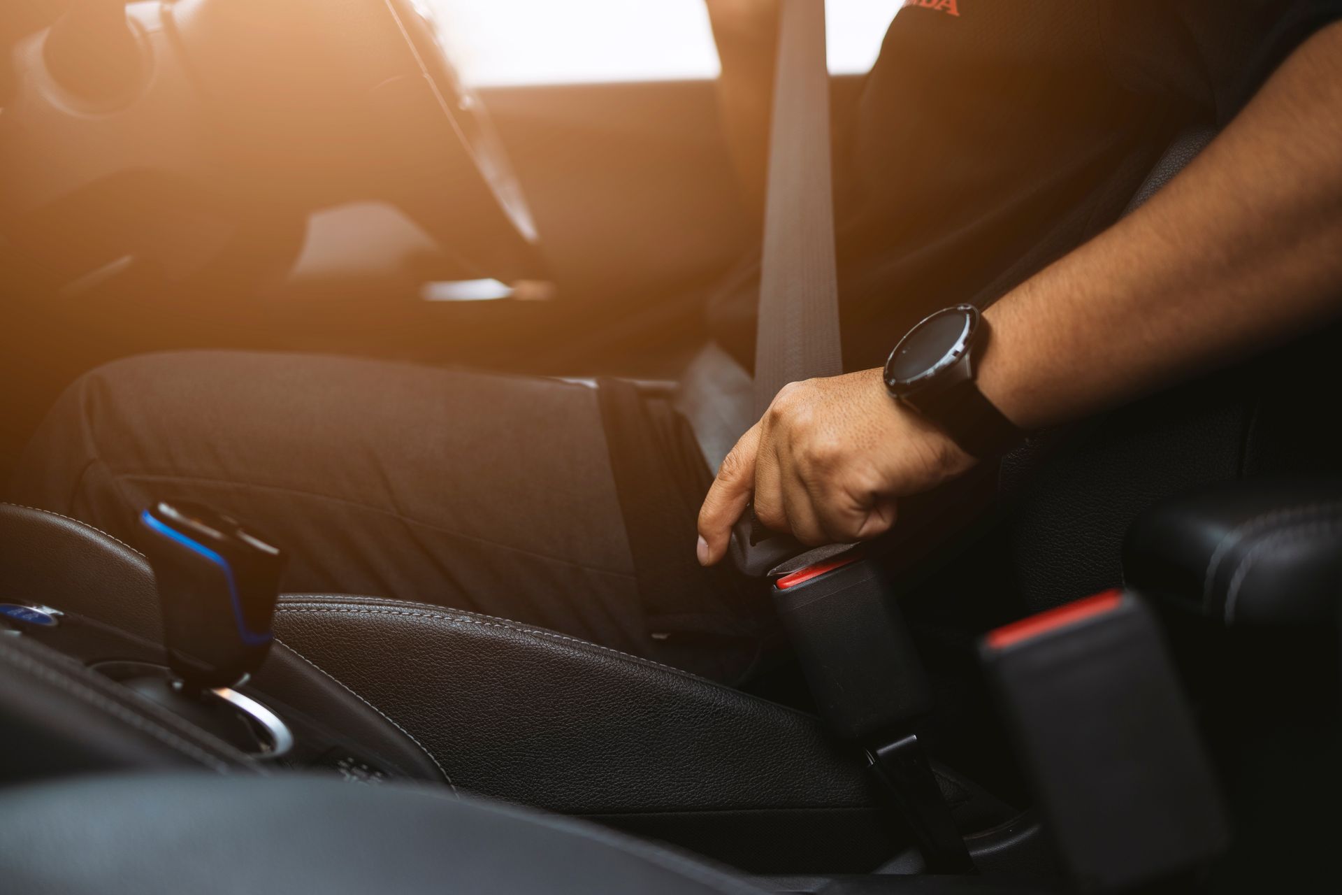 A person's hand wearing a watch fastens a seatbelt in a vehicle.