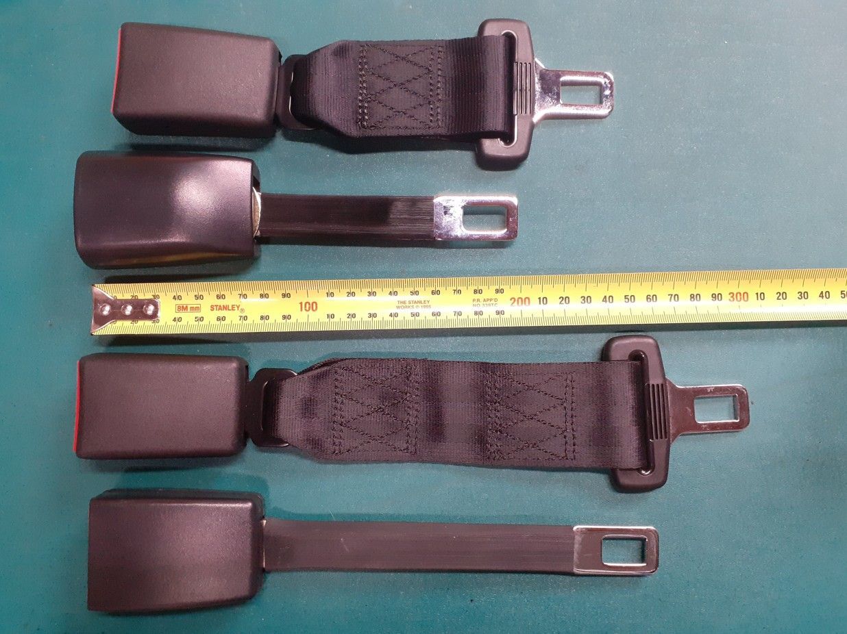 Four black seat belts and buckles laid out on a green background beside a measuring tape
