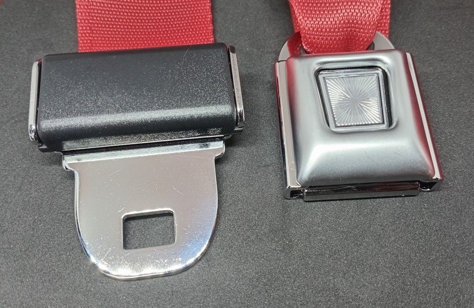 Two red safety straps with metal buckles, one open and one closed on a dark surface