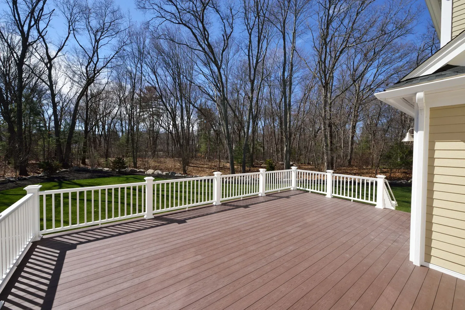 Wooden deck with white railing, overlooking a grassy yard and bare trees.