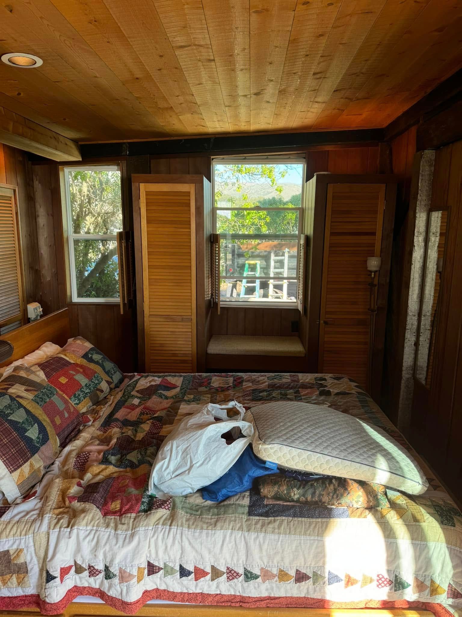 Bedroom with a bed, windows, and wooden paneling. Sunlight streams in.