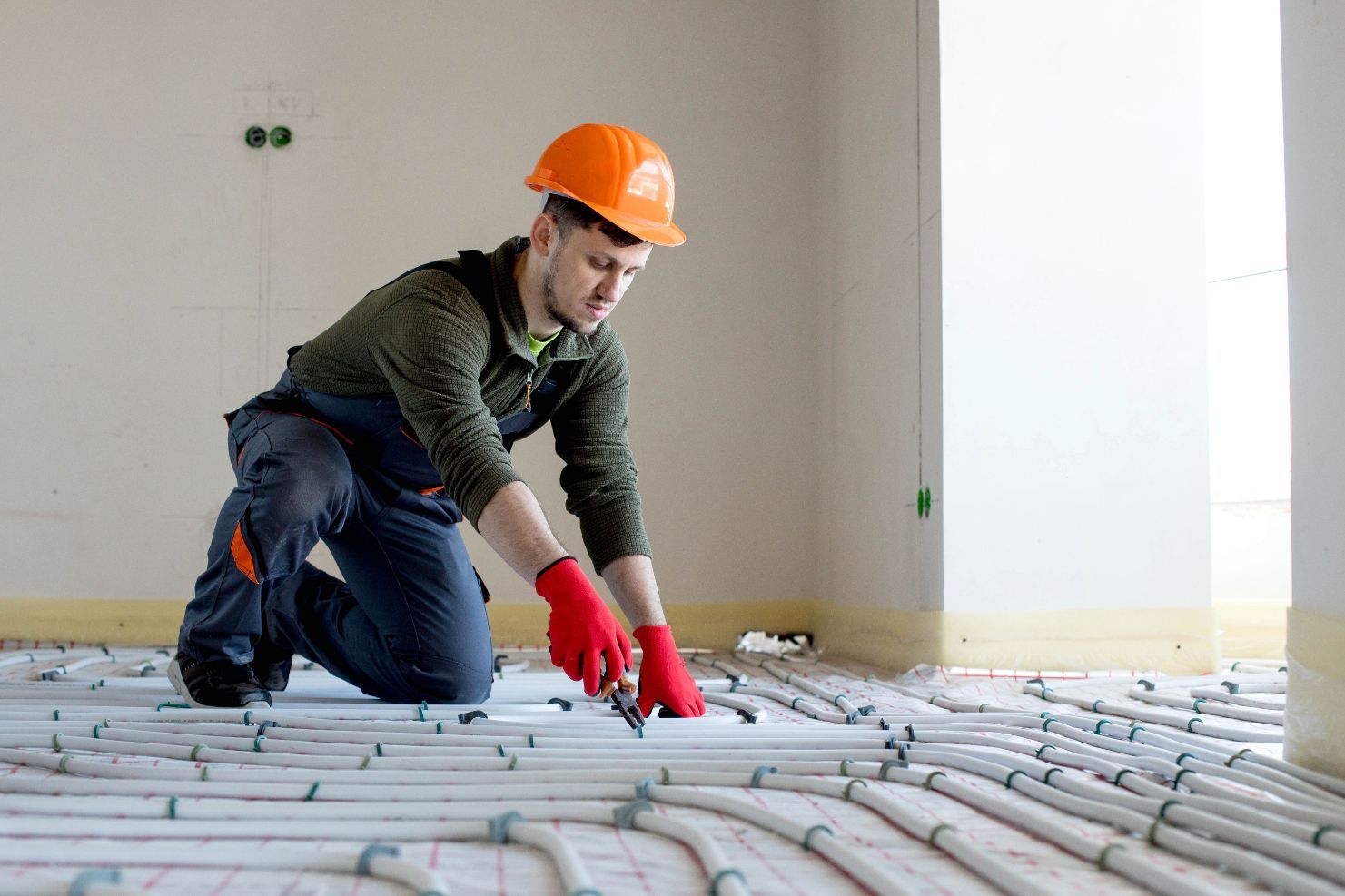 Construction Worker Kneeling and Cutting Pipe — Illawarra Underfloor Heating In Kiama, NSW