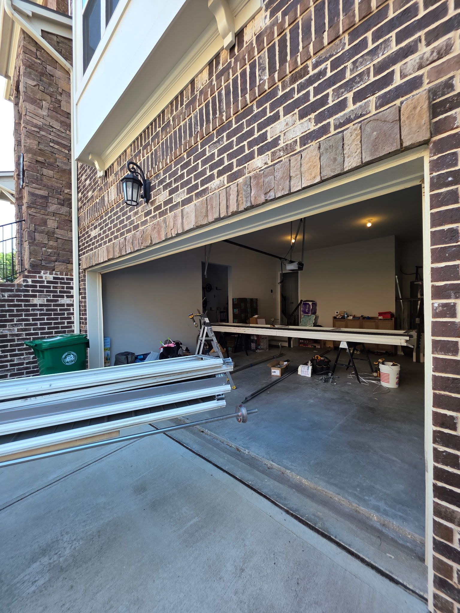 Open garage with stacked metal pipes and tools on the floor in front of a brick house