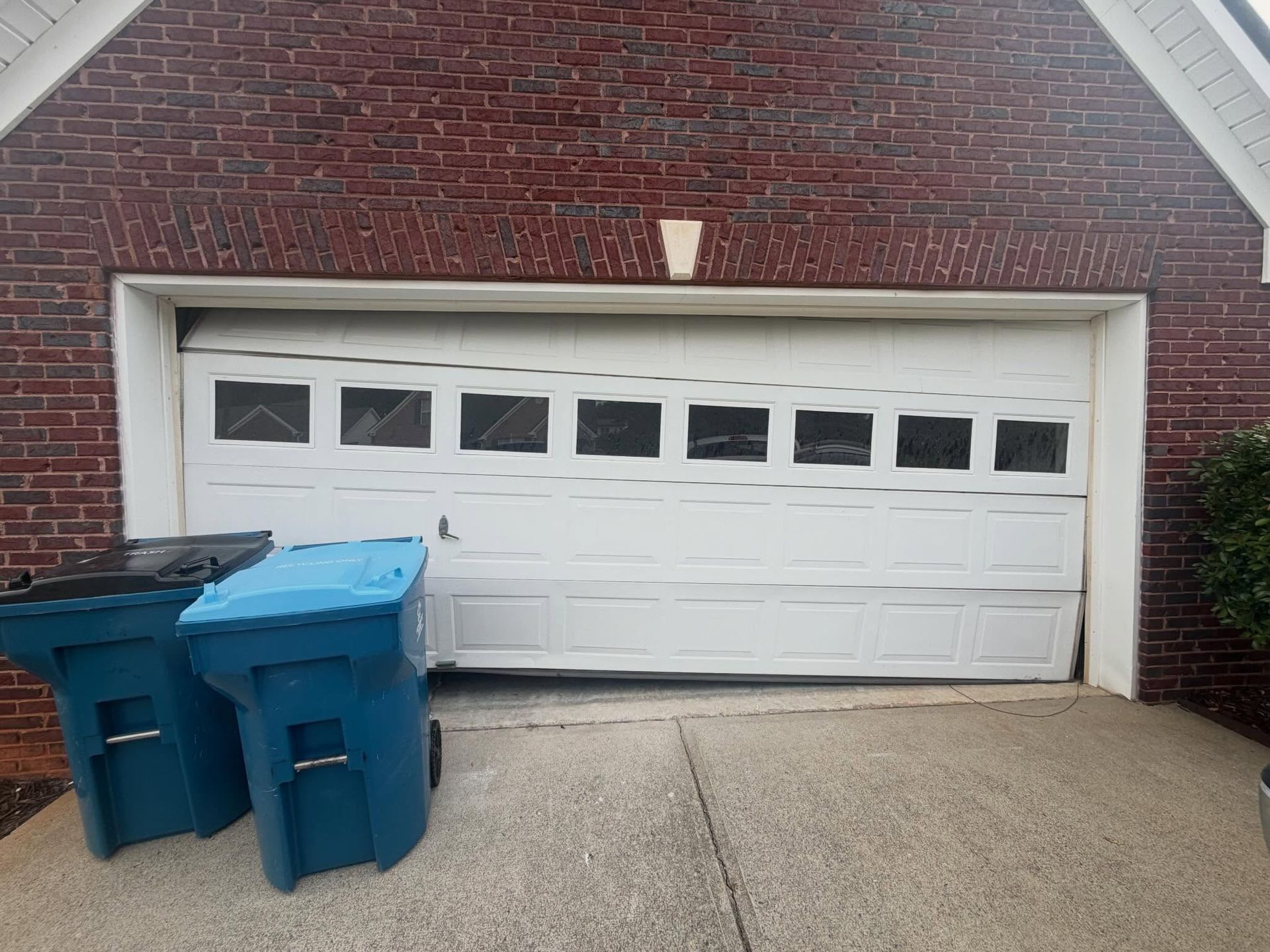 White garage door on a red brick house with two blue trash bins on a concrete driveway