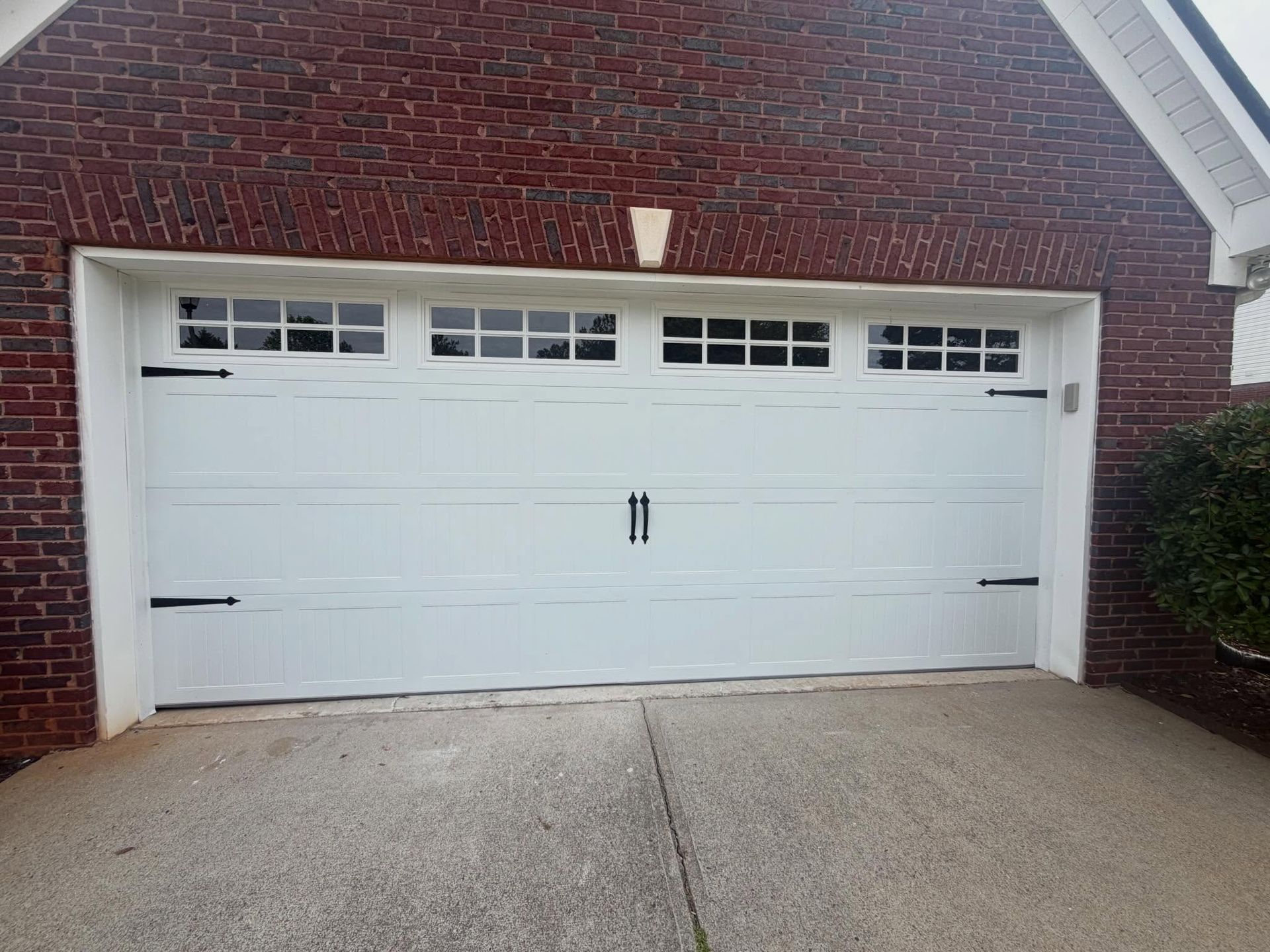 White garage door on a brick house with a concrete driveway and small windows along the top.