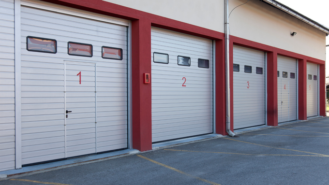 Row of gray garage doors with red trim on a building exterior