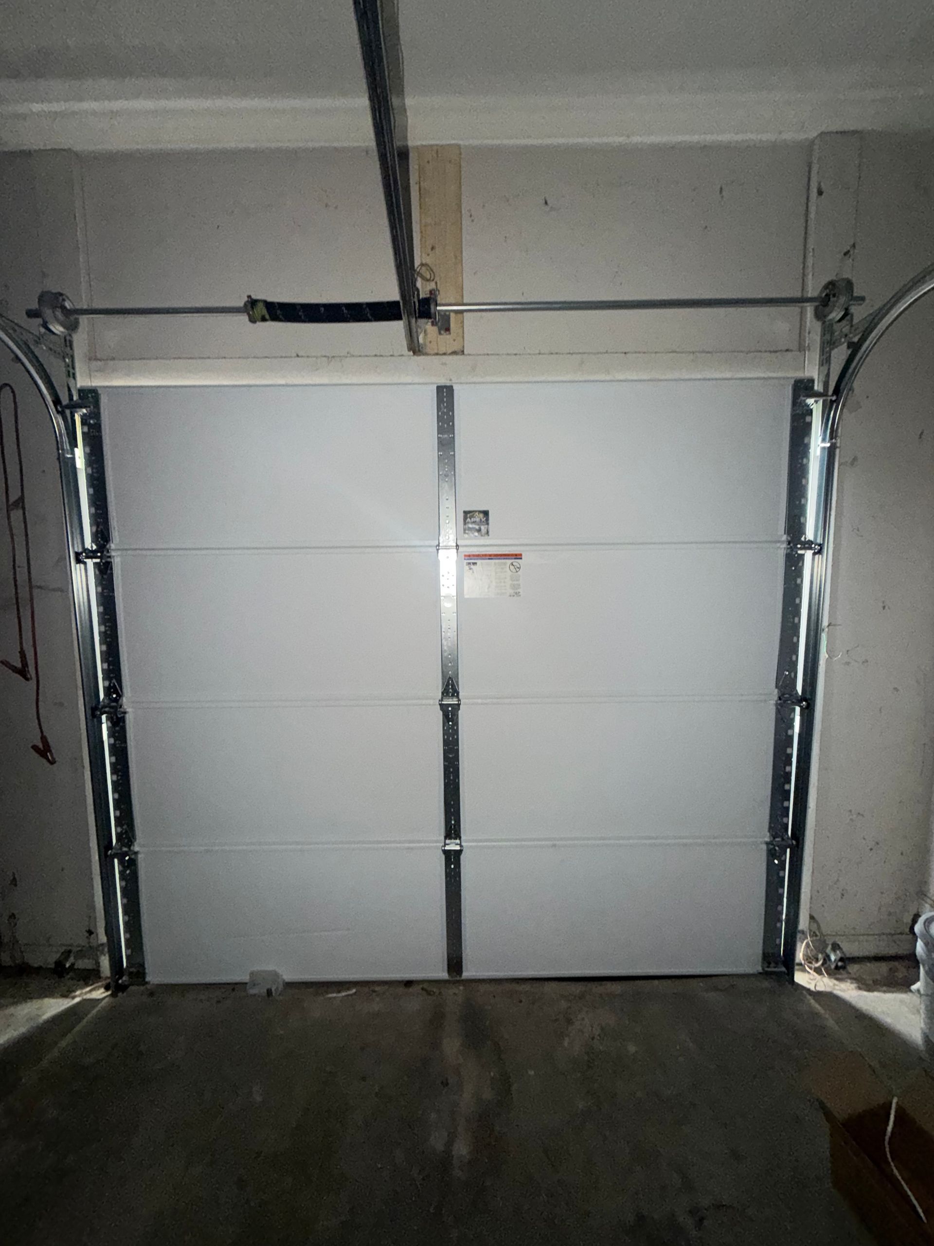 White garage door with a central handle, viewed from inside a dim garage.