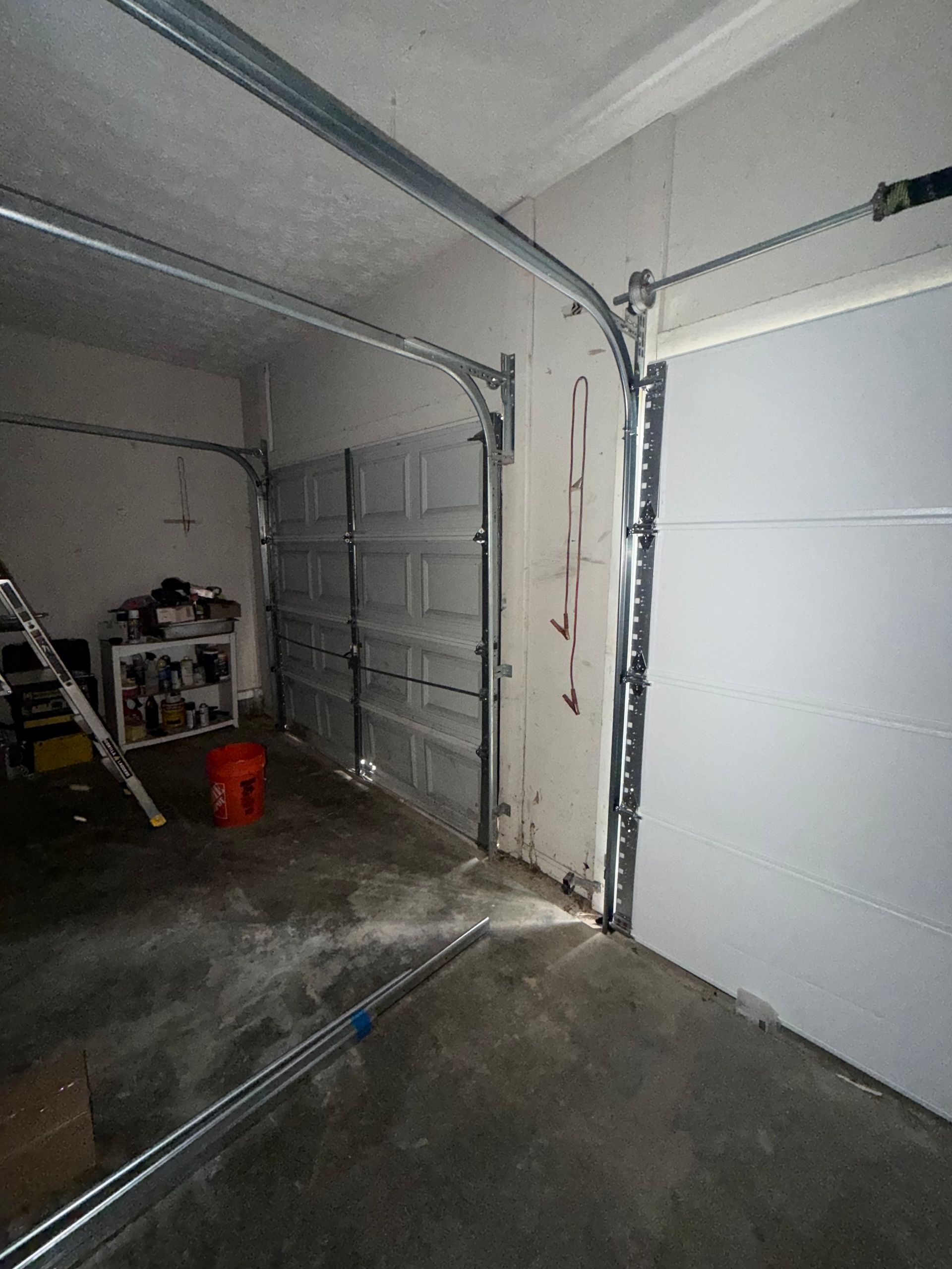 Open garage interior with closed white door, concrete floor, and storage shelves on the left.