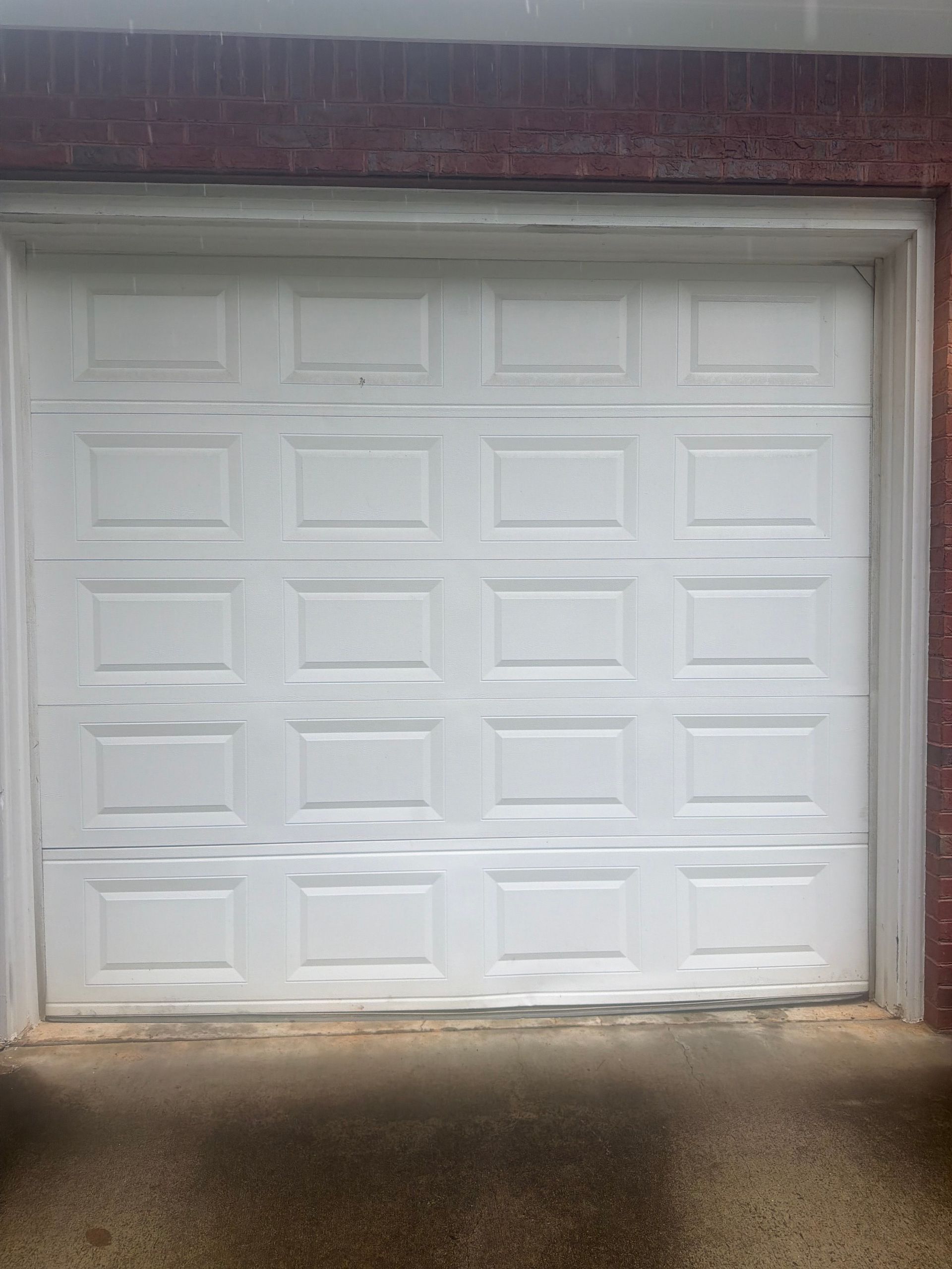 White paneled garage door with a small dent, set in a brick opening with a concrete driveway.
