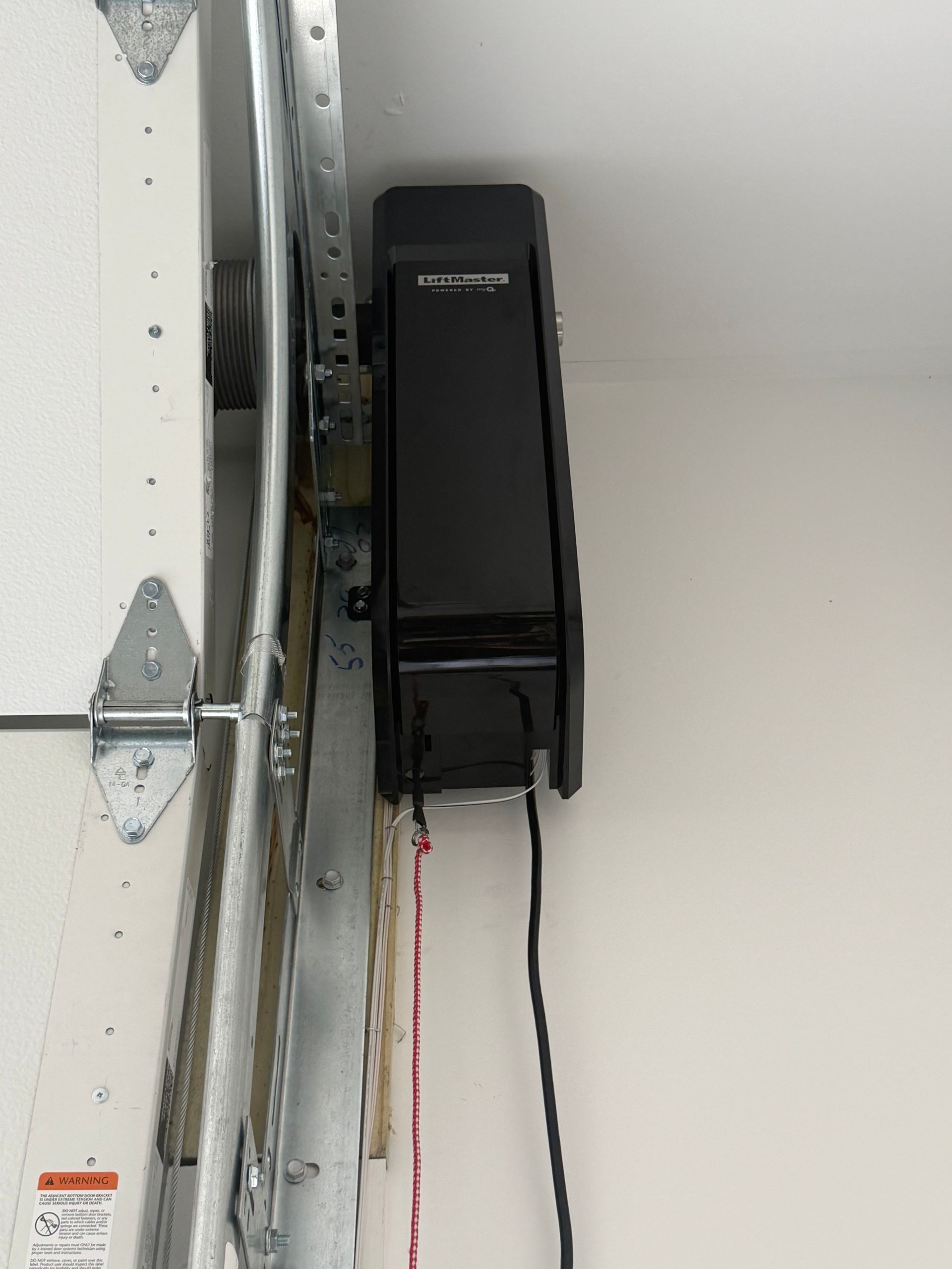Black wall-mounted garage opener unit with hanging cords beside a garage door track