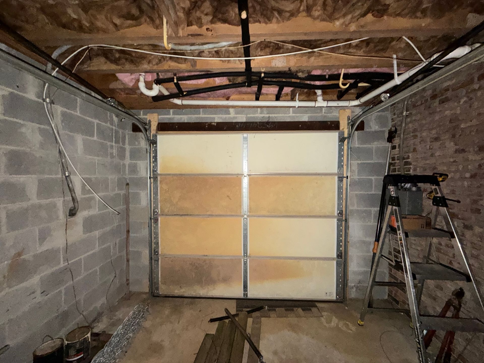 Empty garage under construction with cinderblock walls, exposed ceiling, and a partially open garage door