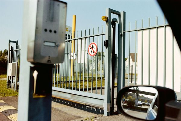 Security gate and fence with a no-entry sign, viewed from a car side mirror