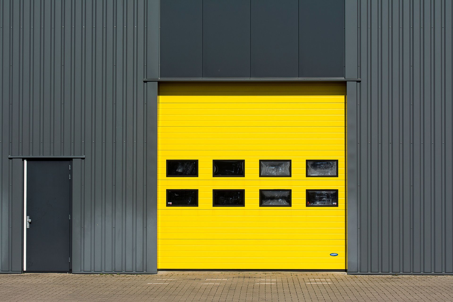 Gray industrial building with a bright yellow garage door and a small gray side door