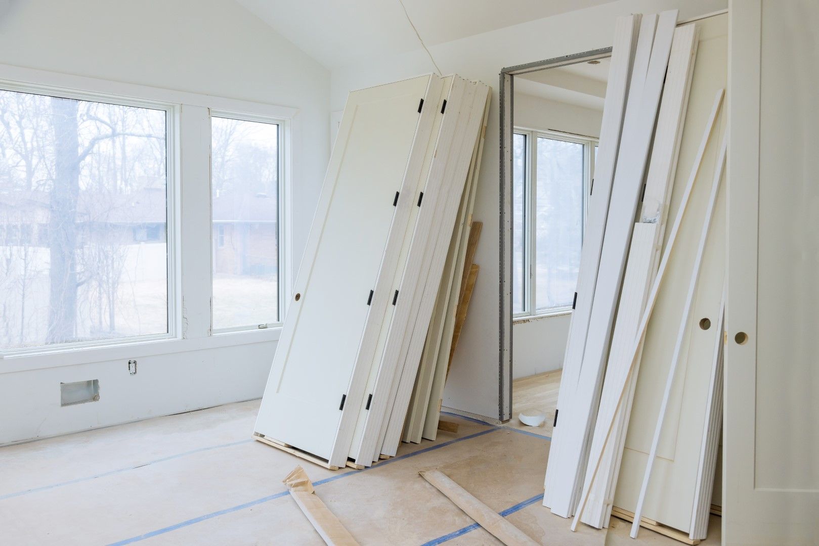 Interior room with white doors and trim stacked against walls during renovation.