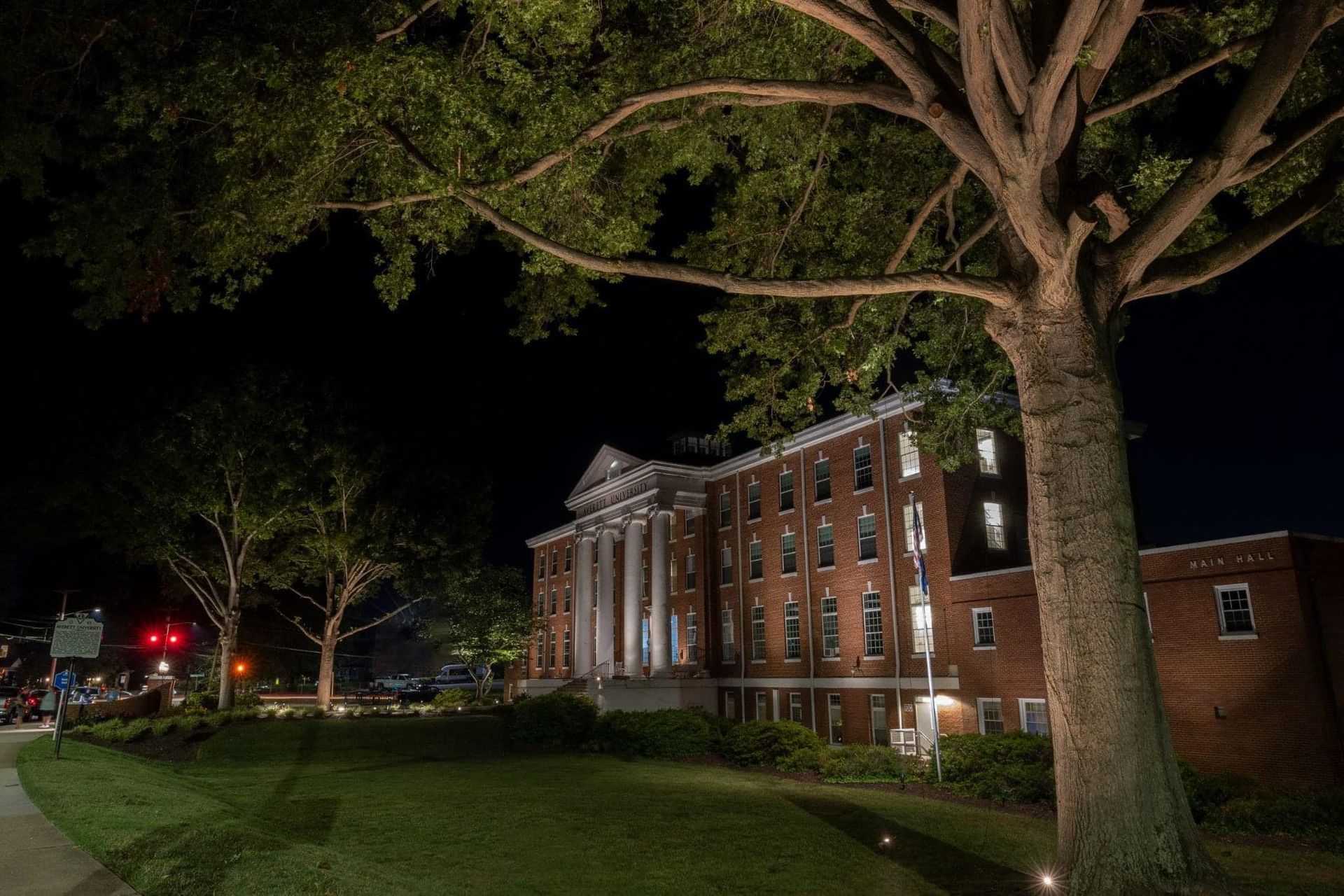 A large brick building is lit up at night with a tree in front of it. A large brick building is lit up at night with a tree in front of it.